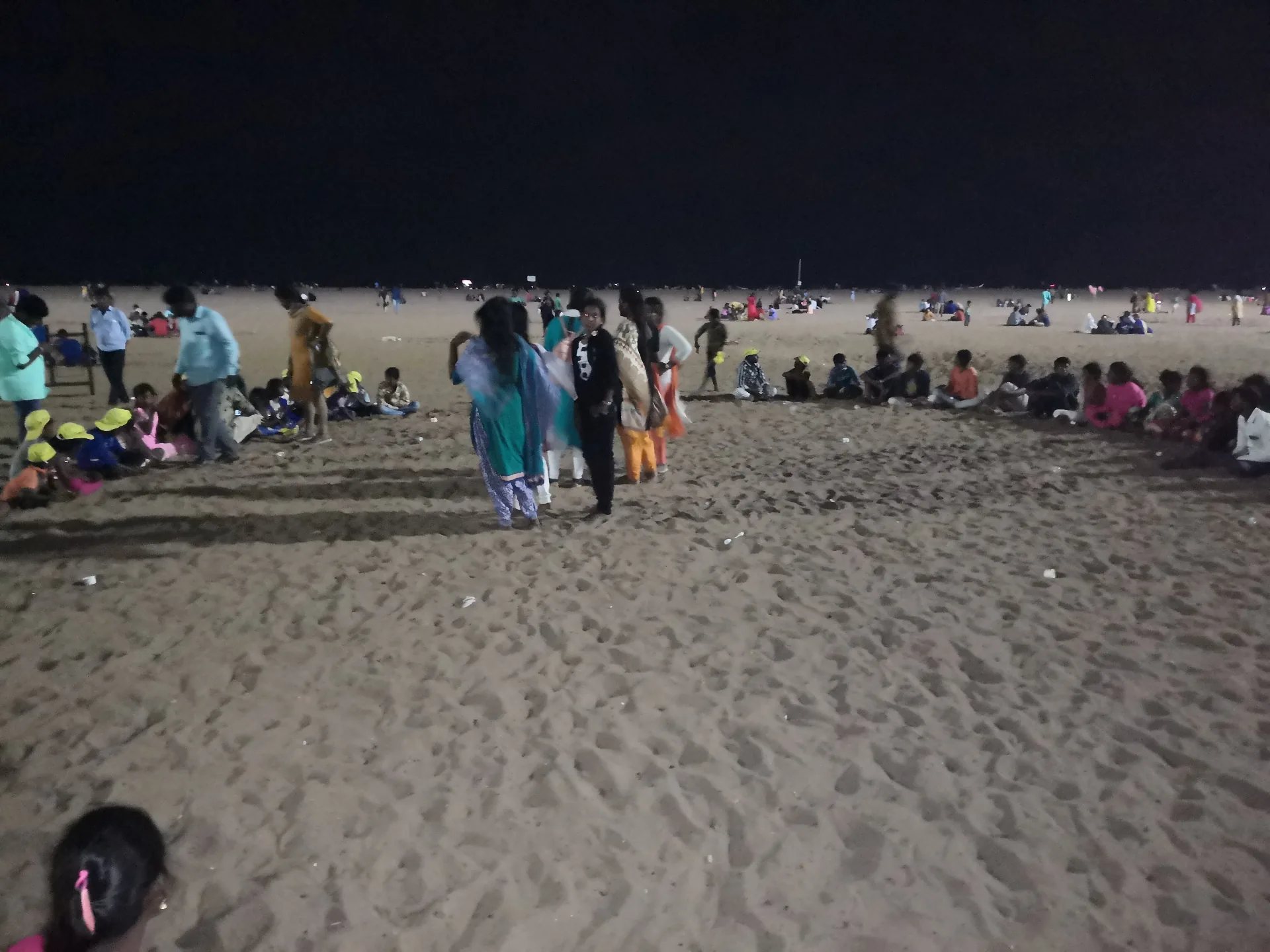 Children in matching yellow caps gathered on the sand at Marina Beach in the evening