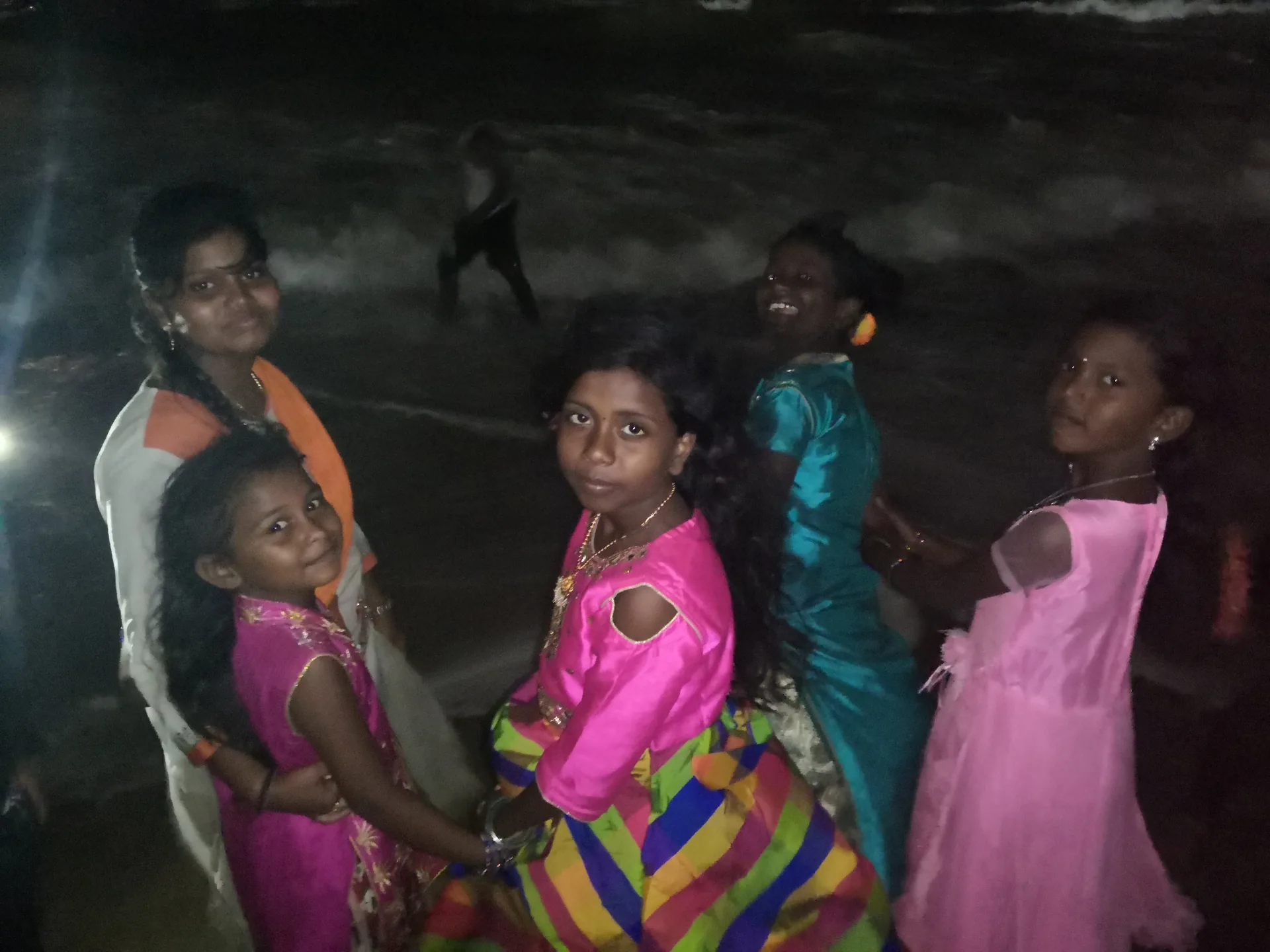 A group of girls in bright dresses smiling by the shoreline at night