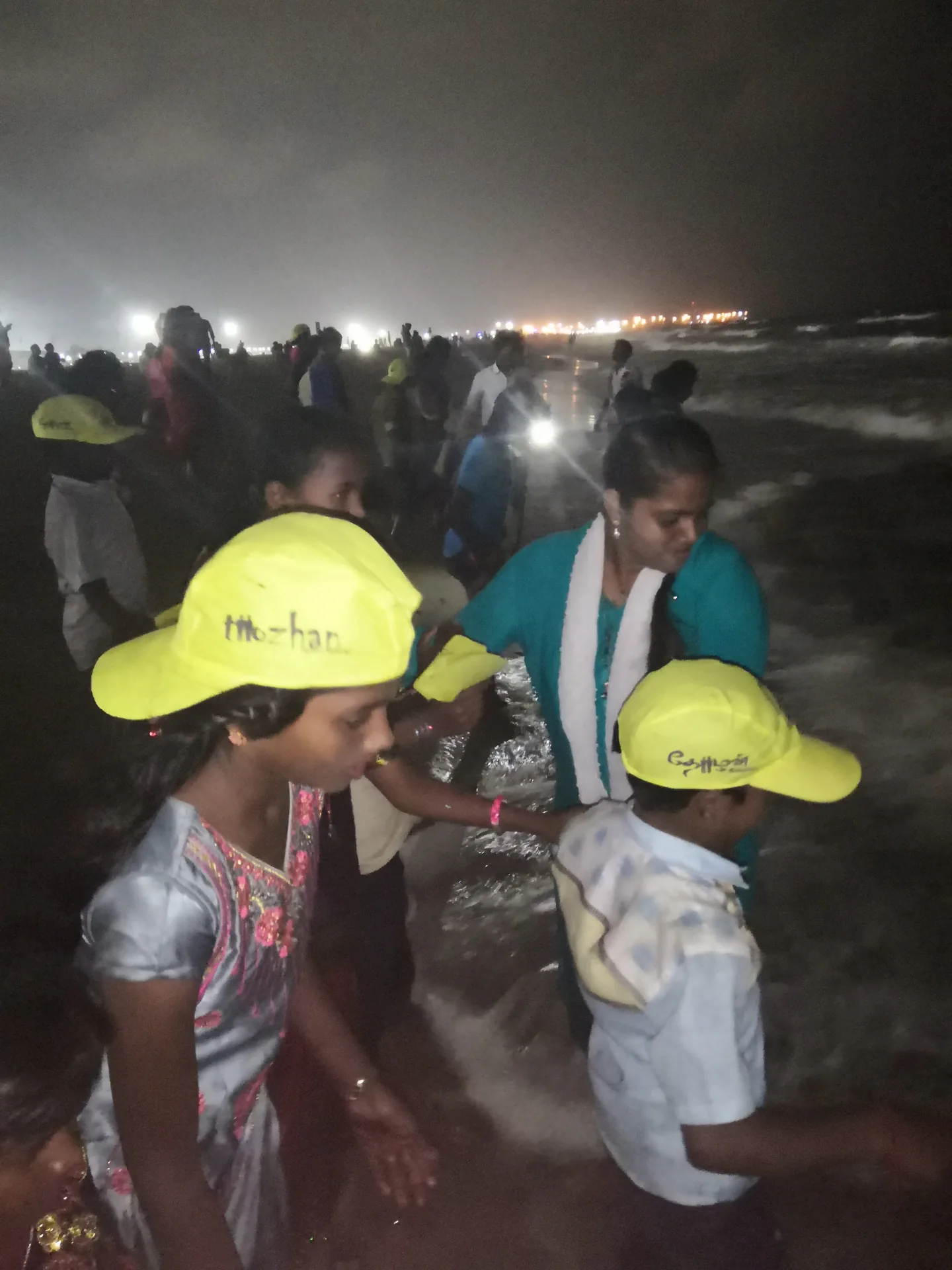 Children with yellow caps stepping into the waves at Marina Beach at night