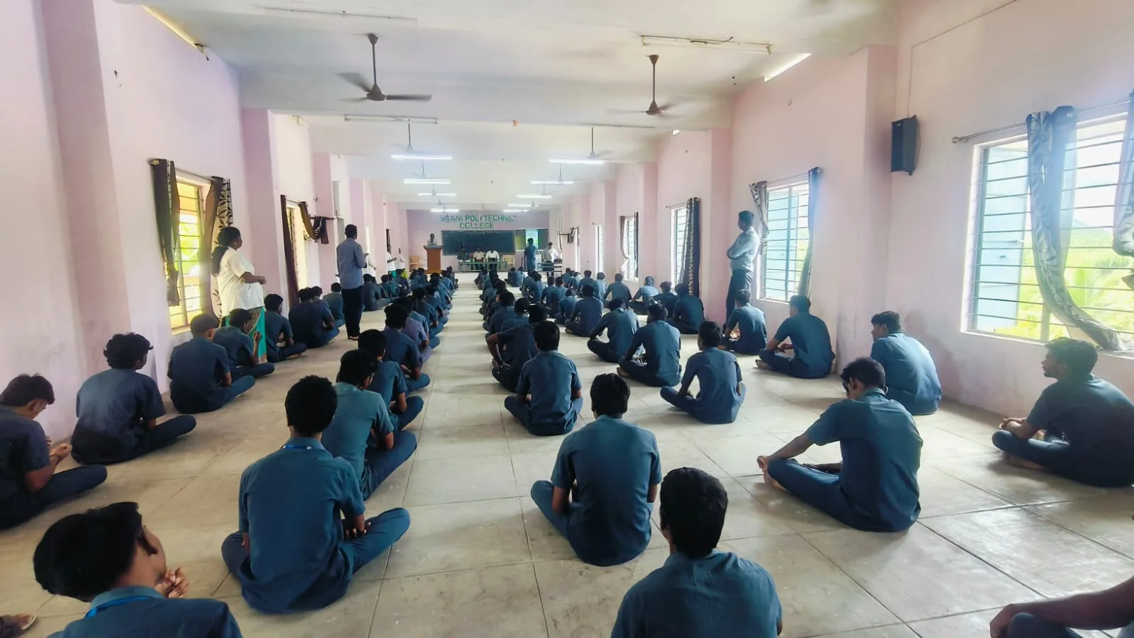 Wide view of students seated cross-legged across the college hall during the yoga and meditation session